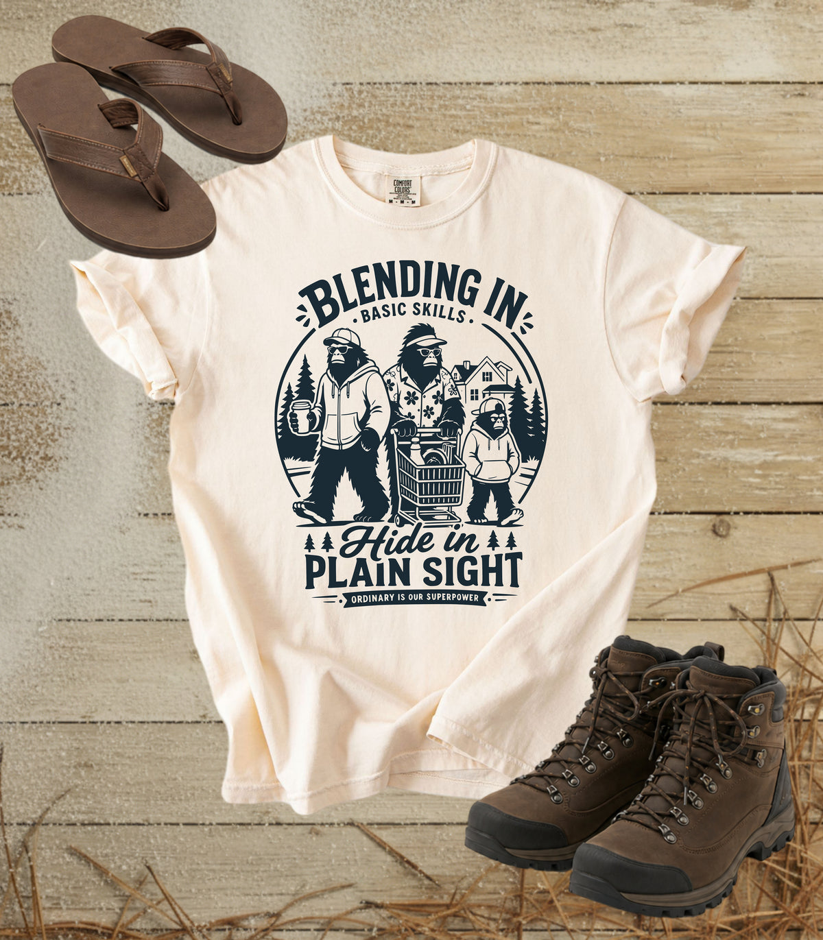 A comfort colors ivory color graphic t-shirt featuring a dark blue bigfoot-themed outdoor print that reads 'Blending In: Basic Skills. Hide in Plain Sight.