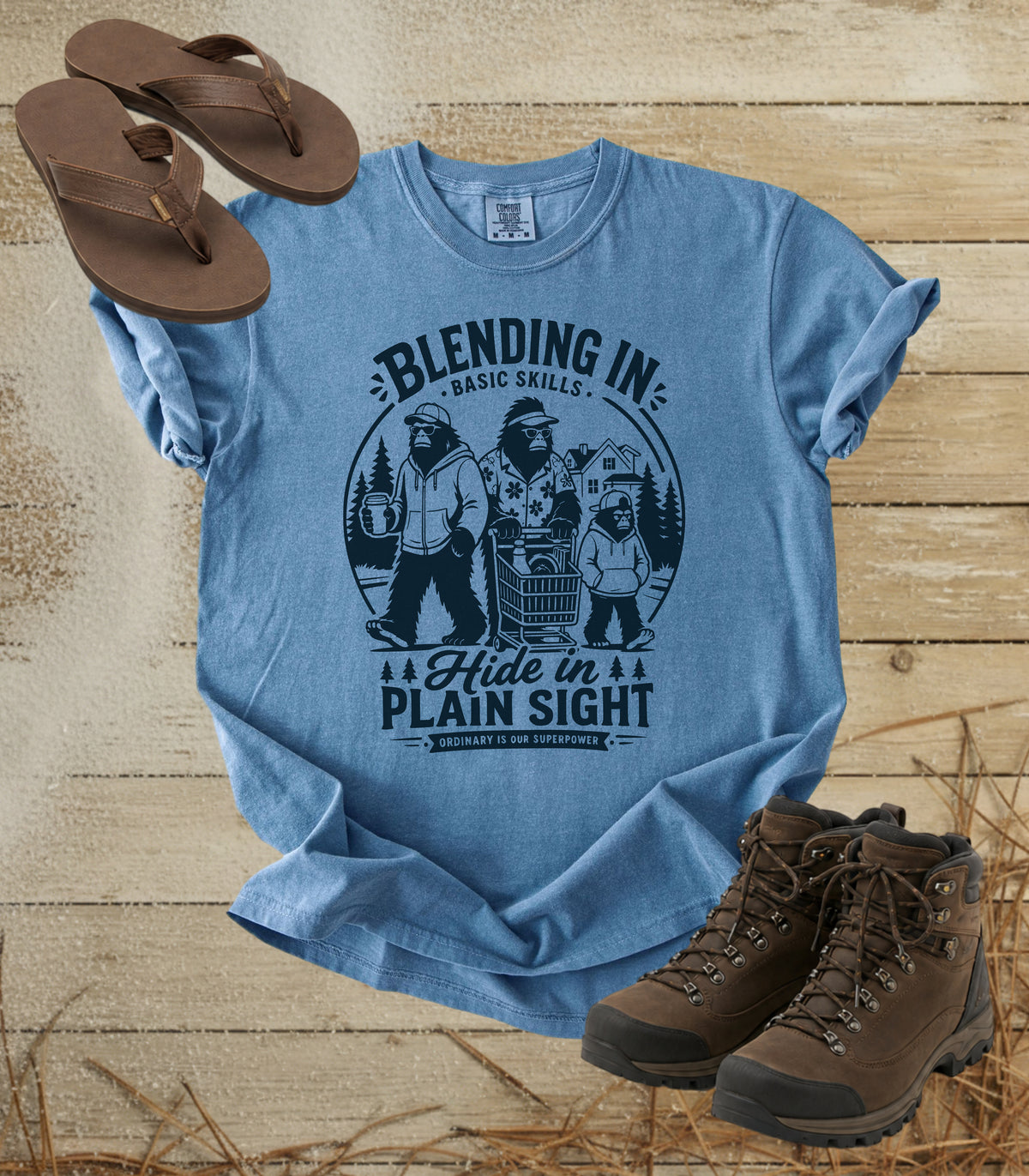 A comfort colors bluejean color graphic t-shirt featuring a dark blue bigfoot-themed outdoor print that reads 'Blending In: Basic Skills. Hide in Plain Sight.