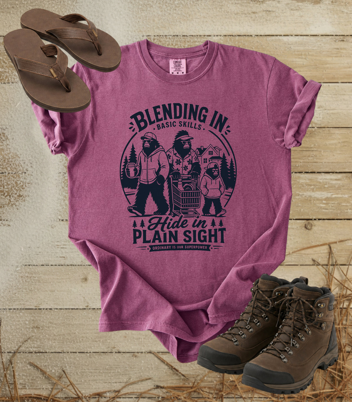A comfort colors berry color graphic t-shirt featuring a dark blue bigfoot-themed outdoor print that reads 'Blending In: Basic Skills. Hide in Plain Sight.