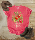 A comfort colors watermelon color short-sleeve graphic T-shirt laid flat on a rustic wood plank surface, styled with brown flip-flops, hiking boots, and straw. The shirt features a watercolor-style tomato plant graphic with green leaves, red tomatoes, and the words 'farm fresh' in white script.